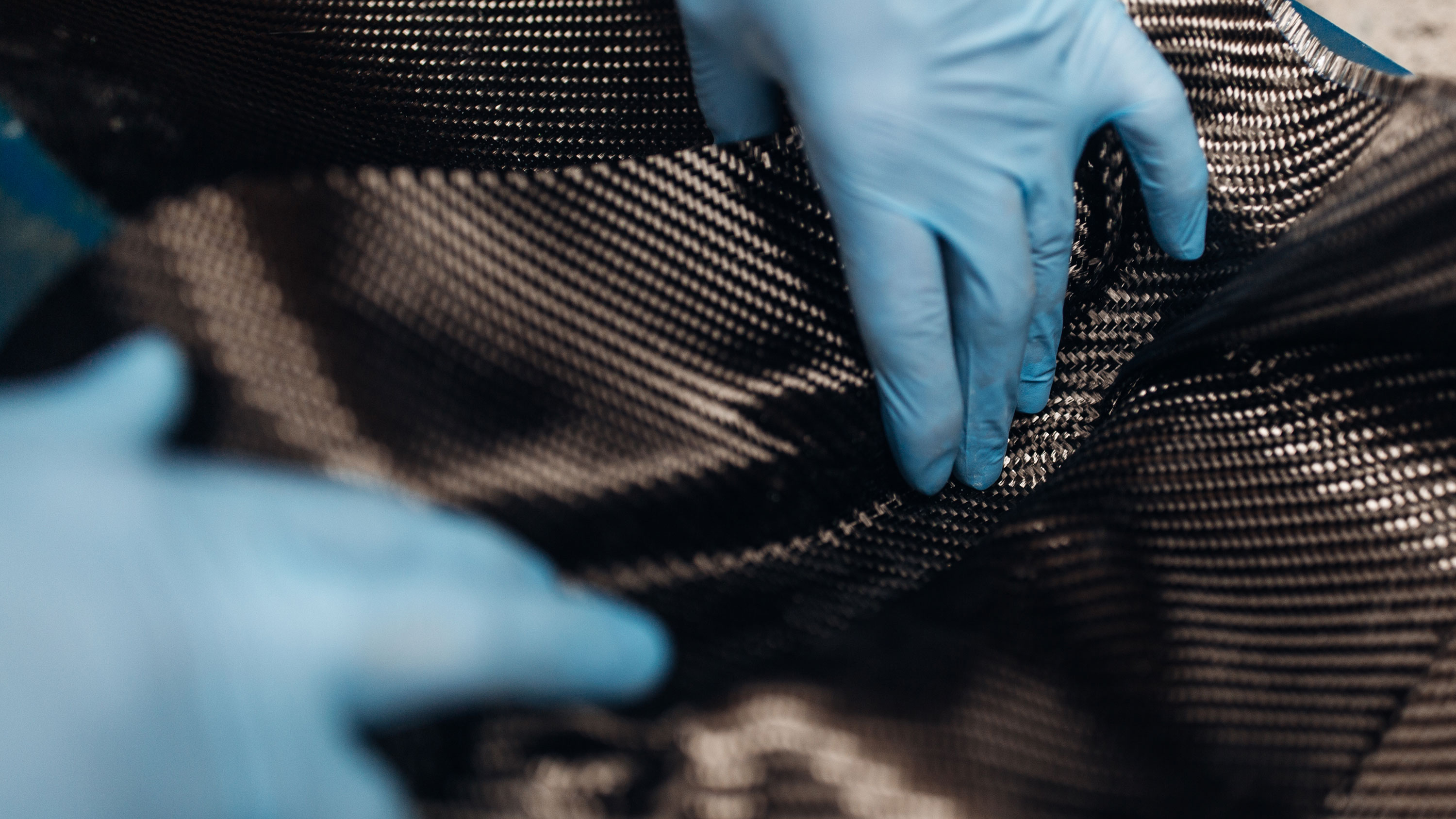 Close up of person wearing gloves making parts from carbon fibre material